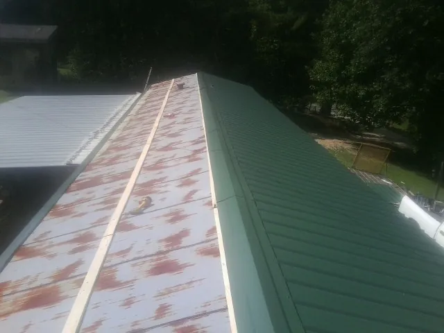 Old rusted panels beside newly installed green metal roofing in Warren
